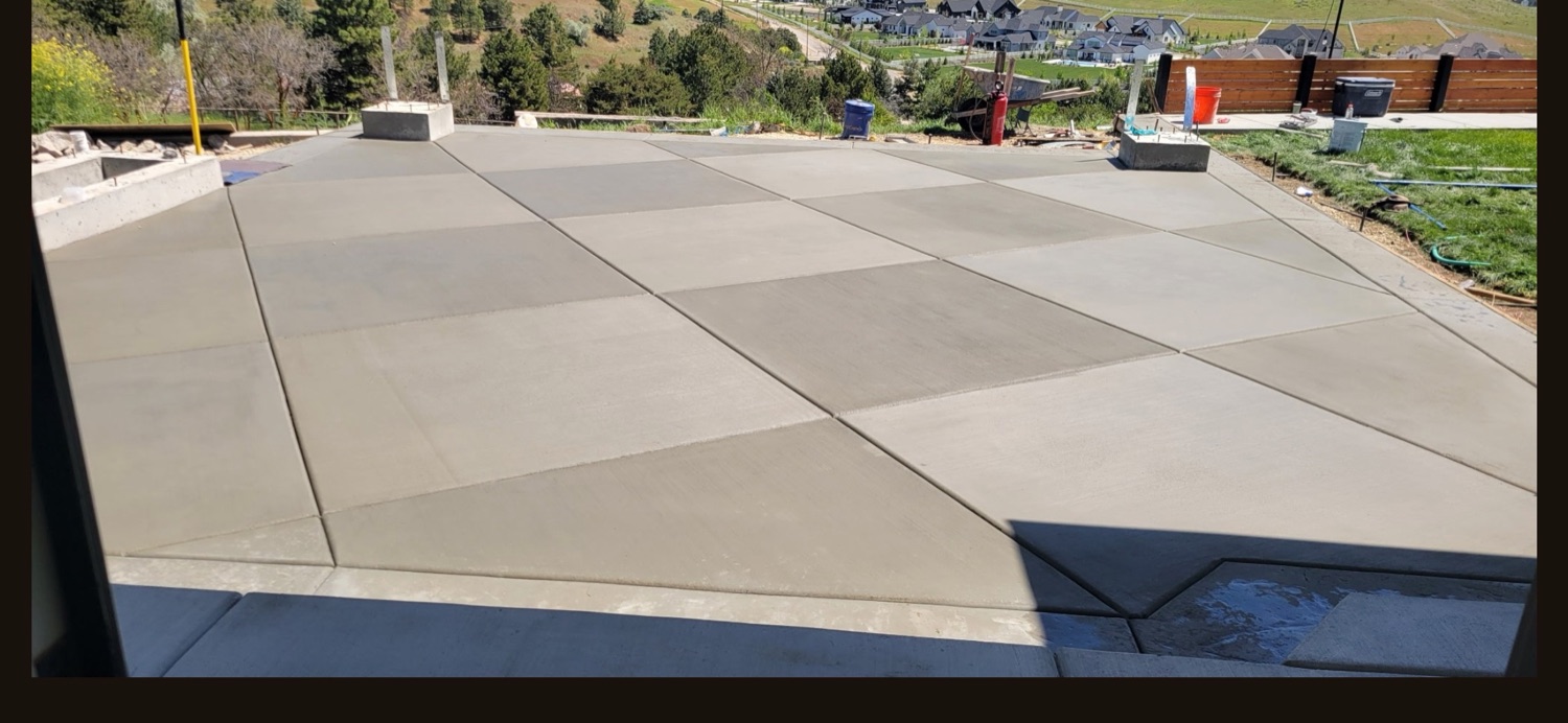 Large finished concrete patio slab with a clean control-joint grid overlooking a hillside subdivision