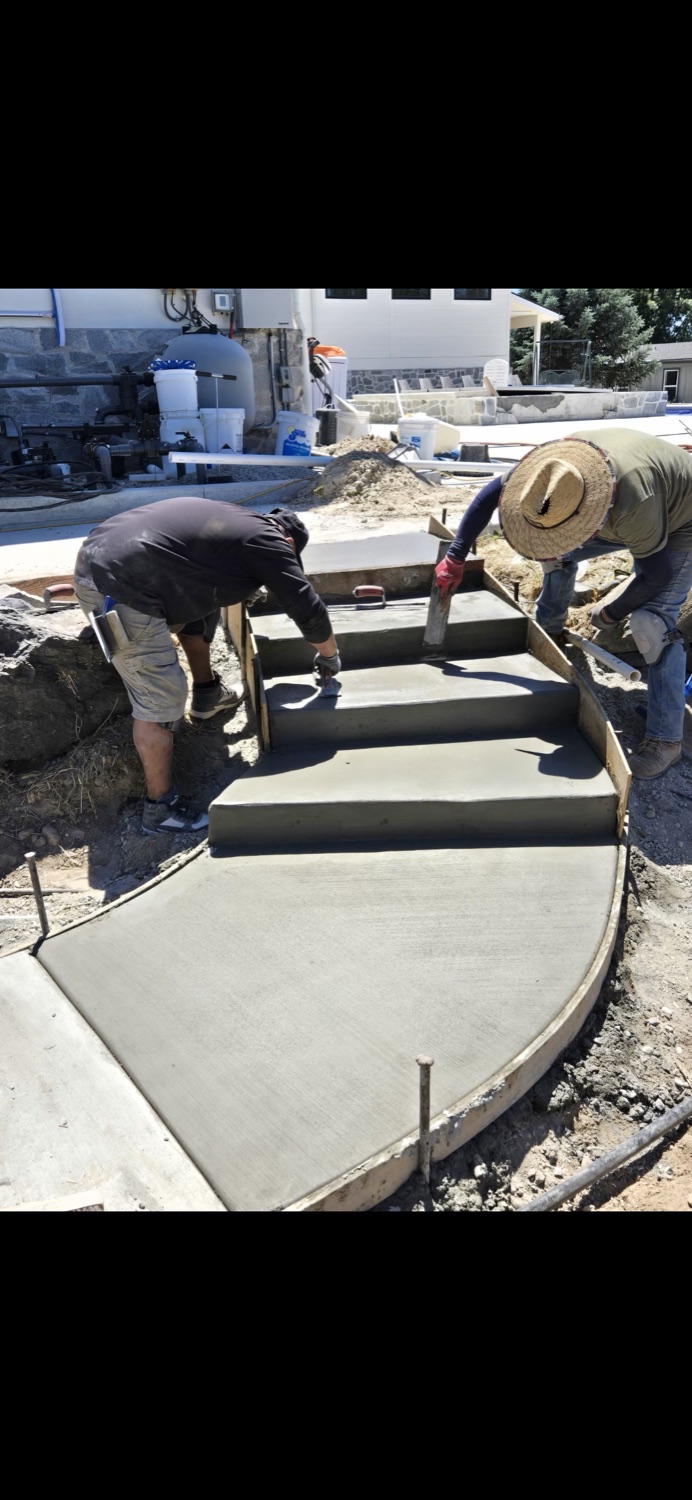 Two Groundworks crew members forming and finishing a curved concrete walkway and steps beside a pool