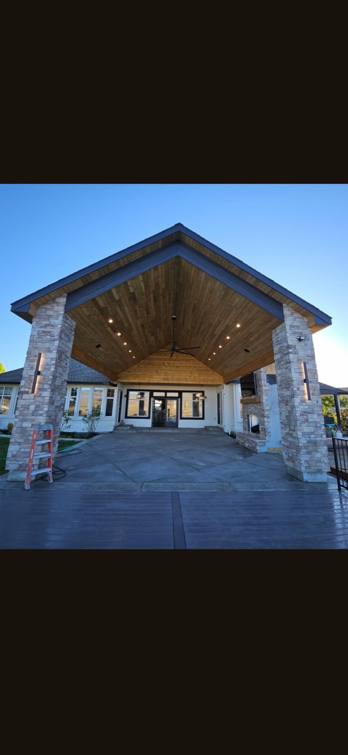 Finished covered outdoor patio with a wood cathedral ceiling, stone columns, and stamped concrete flooring on a custom home